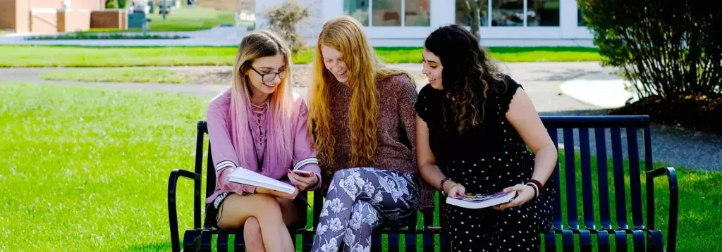 Three female students sitting on a bench looking at a textbook